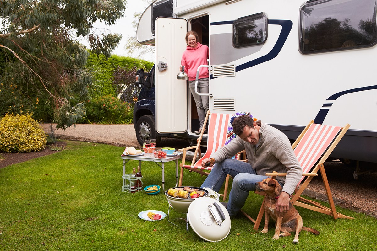  Un couple devant un camping-car au barbecue.